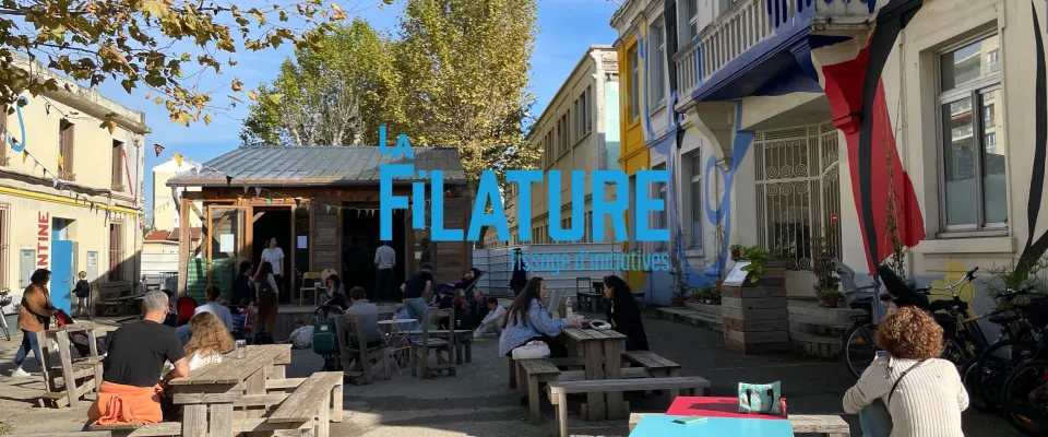 La cour de La Filature, avec des tables où des personnes discutent au soleil.